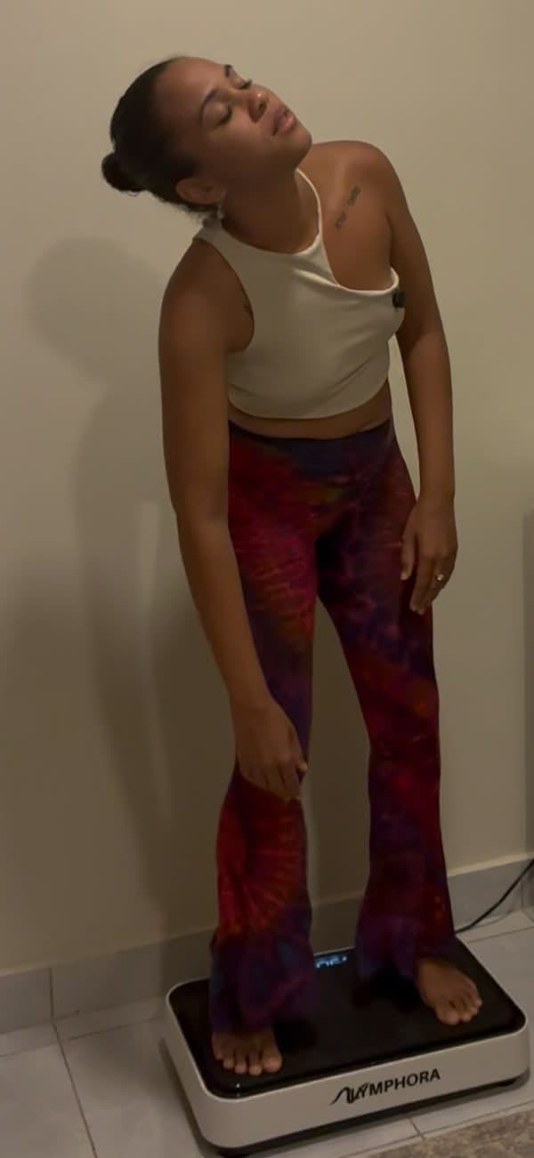 A person standing on a whole-body vibration plate, leaning into a gentle side stretch.