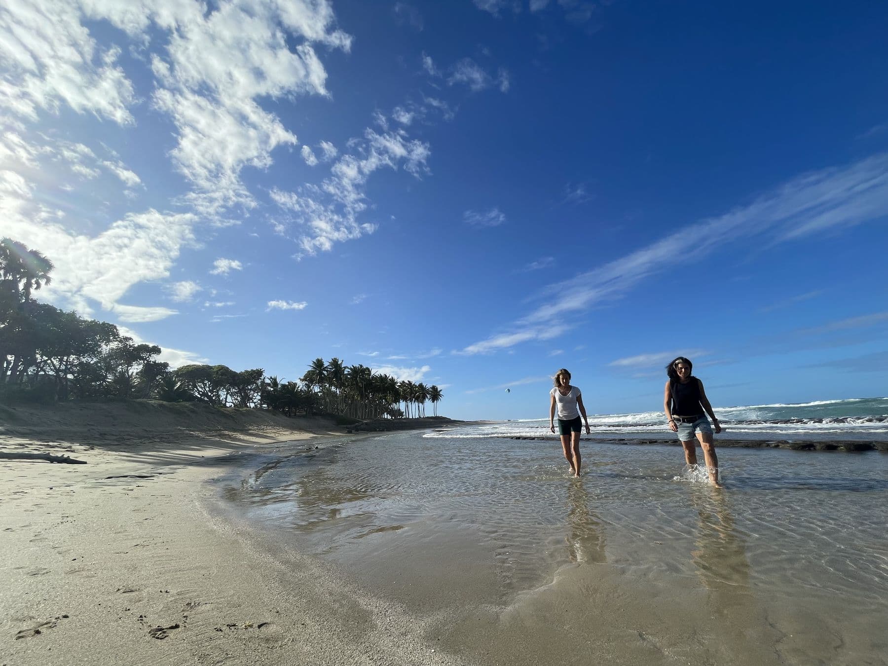 Two people walking through shallow water on a wide beach beneath a huge sky.