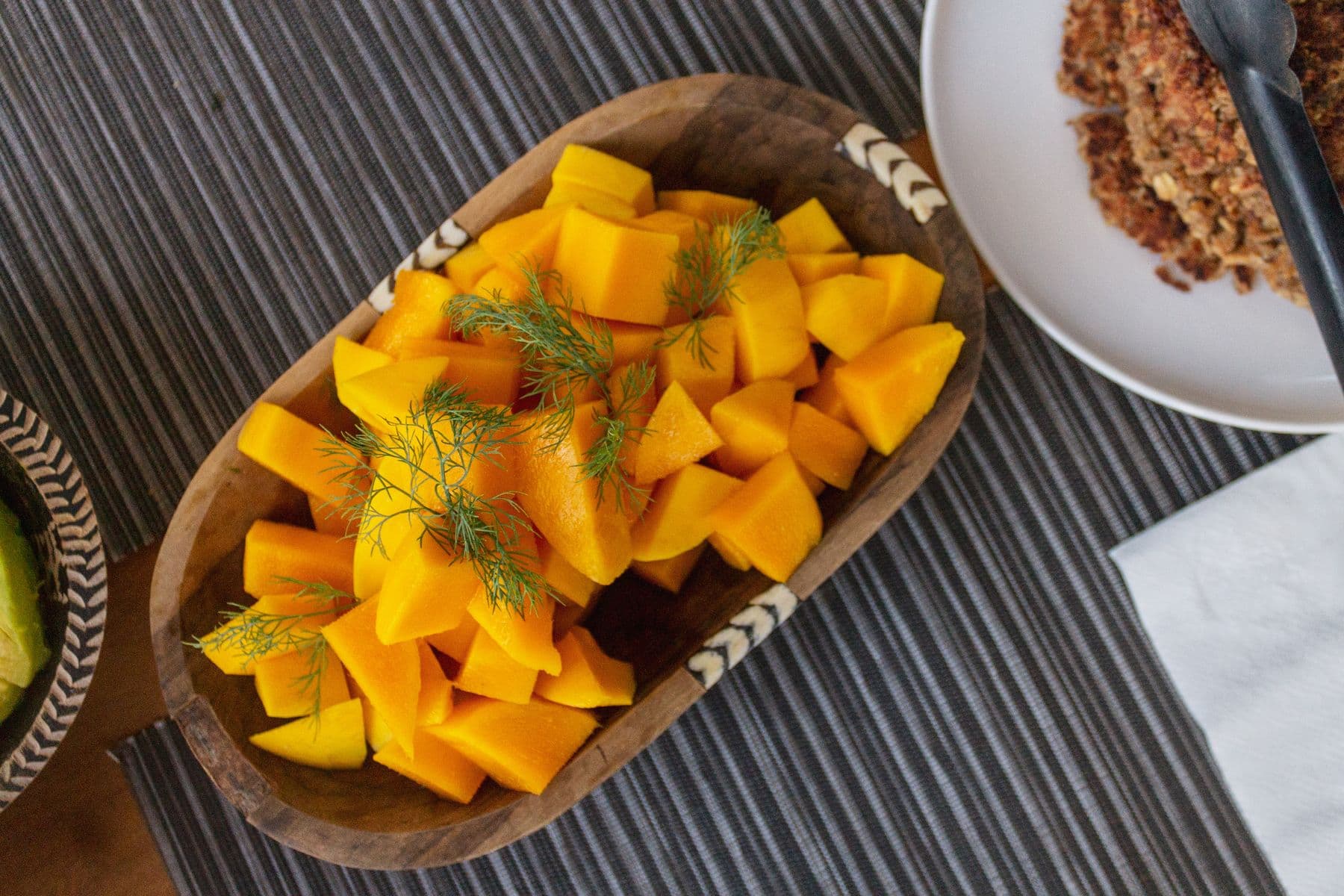 Fresh mango pieces with dill in a carved wooden bowl.