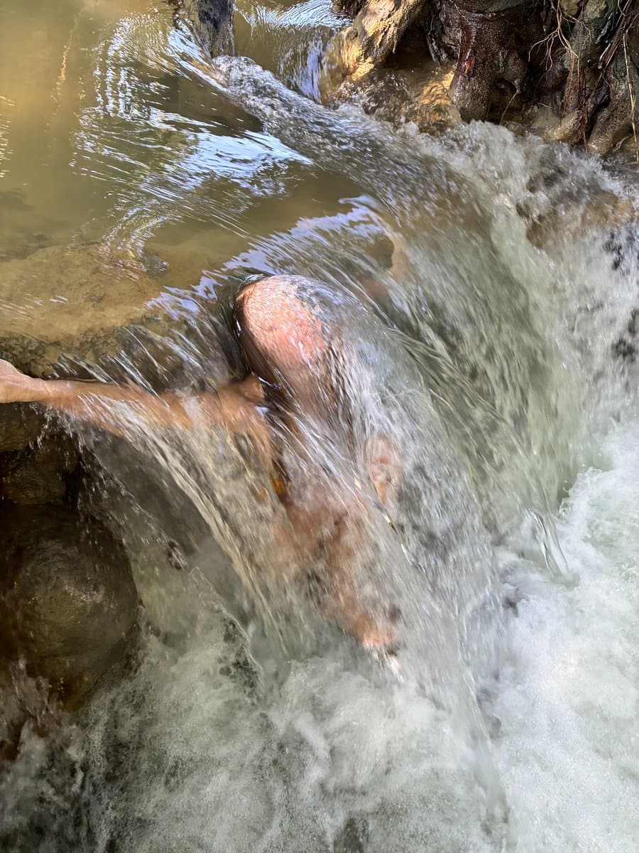 A swimmer partly visible beneath a rush of river water pouring over rocks.