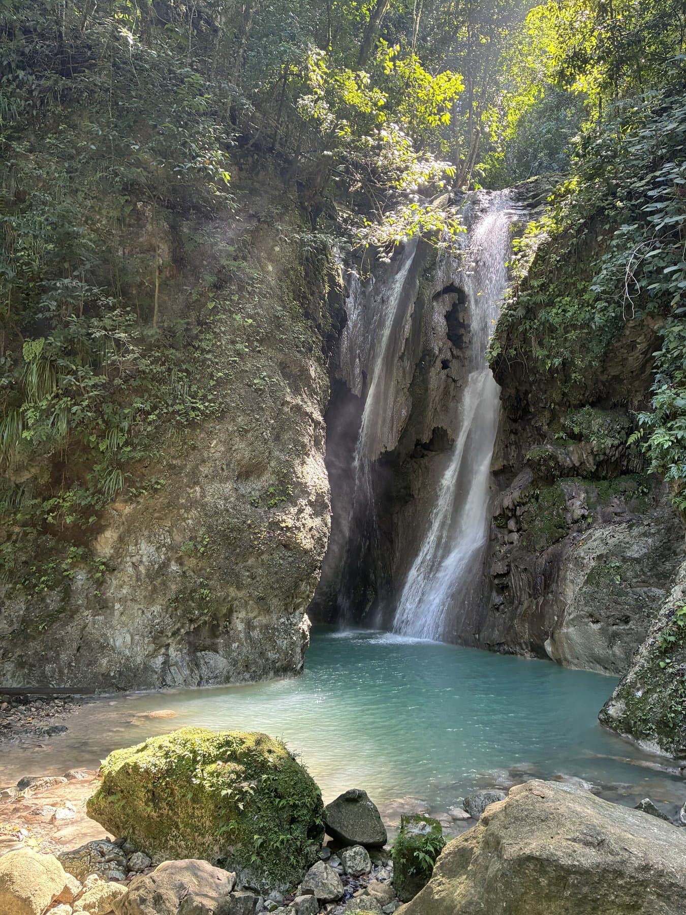 A waterfall dropping into a turquoise pool, surrounded by green forest.